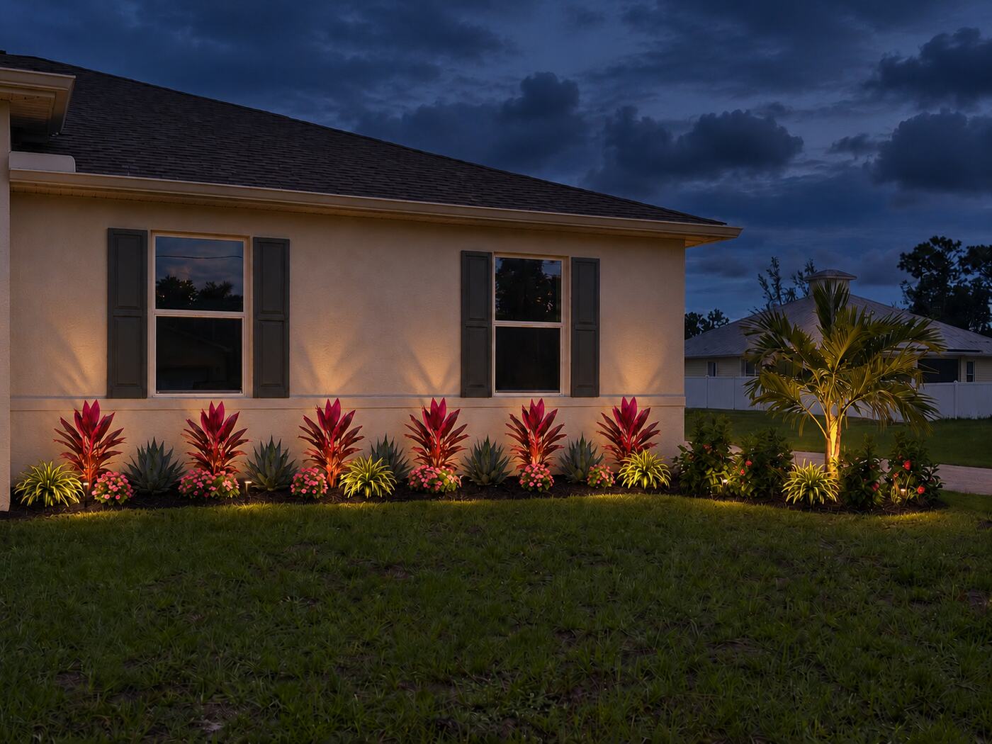 Foundation bed of red ti plants, agave and flowers with landscape lighting at dusk
