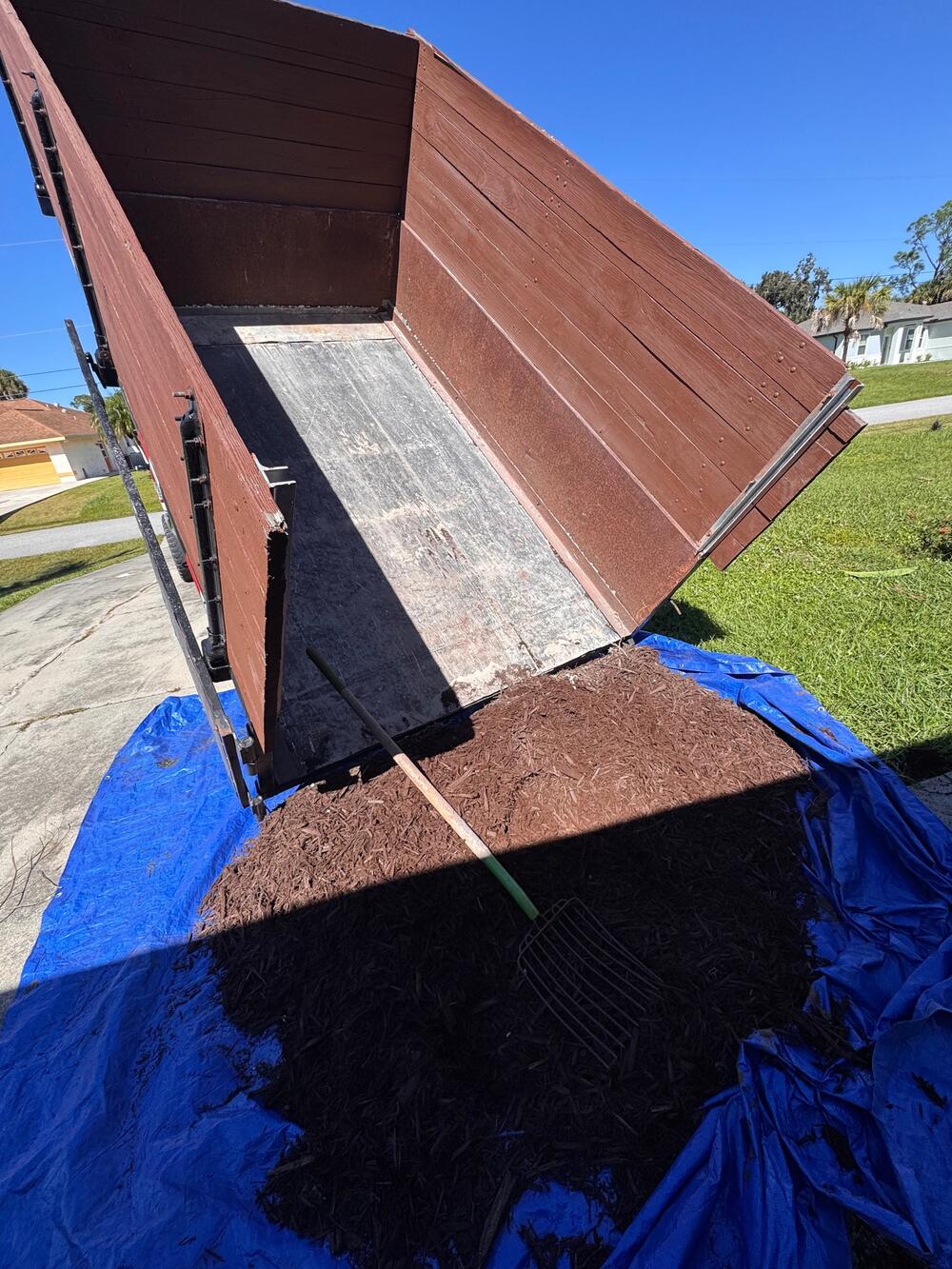 Dump trailer unloading a fresh load of brown mulch onto a tarp